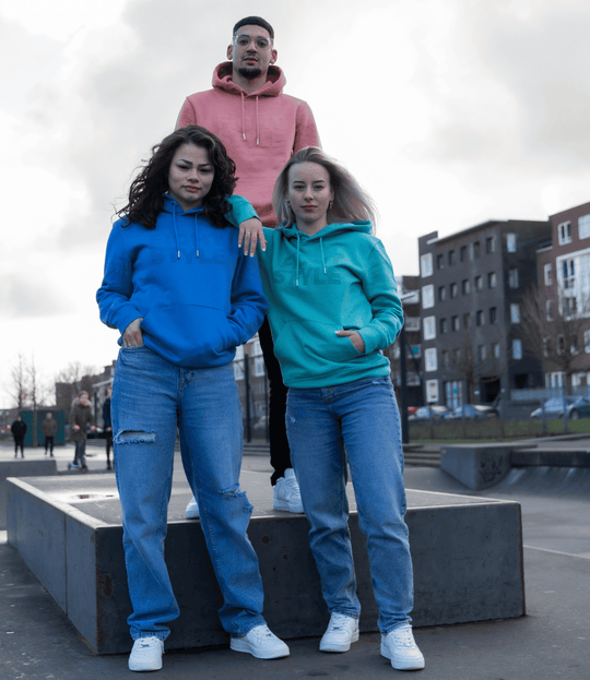 Drie modellen dragen Fightstyle hoodies in blauw, teal en koraalroze tijdens een fotoshoot in het skatepark. De hoodies hebben een moderne fit en een clean logo-design, perfect voor fighters die stijl en comfort willen combineren.