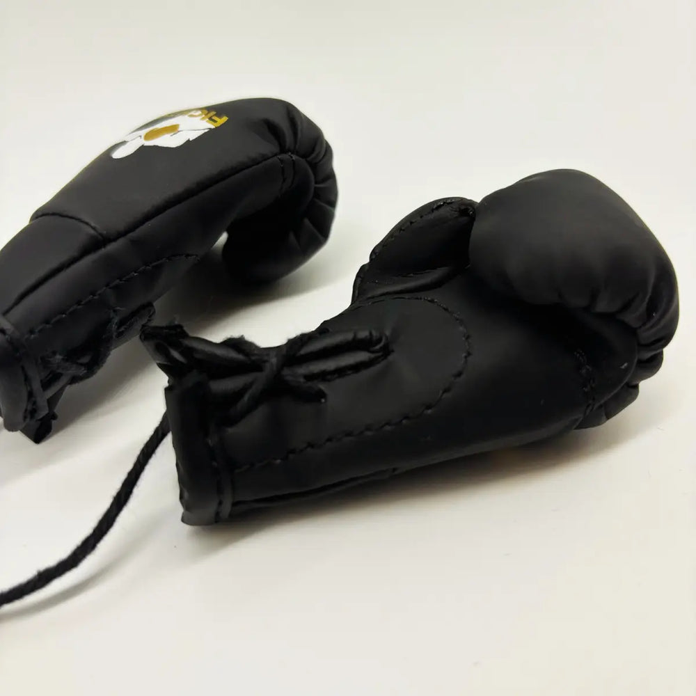 Close-up van zwarte Fightstyle mini bokshandschoenen met veterdetail, gebruikt als decoratie of sleutelhanger.
