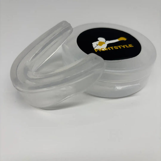 Detailfoto van de transparante Fightstyle mondbeschermer naast het opbergdoosje, ideaal voor bescherming tijdens boksen en kickboksen.
