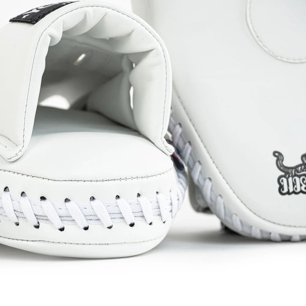 Close-up van Yokkao focus mitt in wit met gewatteerde handinvoer en witte veters aan de onderzijde. De stevige stiksels en zwarte accenten zijn zichtbaar tegen de witte buitenzijde. Detailopname van de afwerking voor bokstraining en Muay Thai padsessies in de gym.