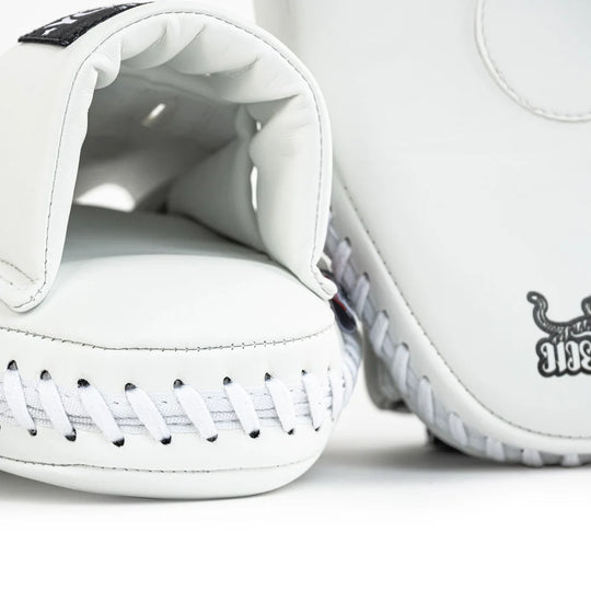 Close-up van Yokkao focus mitt in wit met gewatteerde handinvoer en witte veters aan de onderzijde. De stevige stiksels en zwarte accenten zijn zichtbaar tegen de witte buitenzijde. Detailopname van de afwerking voor bokstraining en Muay Thai padsessies in de gym.