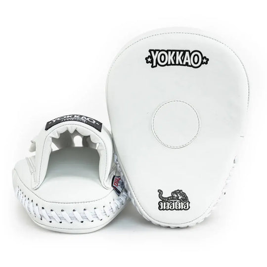 Yokkao focus mitts in wit met zwarte logo-opdruk, gefotografeerd tegen een neutrale witte achtergrond. Rechts is de voorzijde zichtbaar met rond doelvlak en Muay Thai-embleem, links de open handinvoer met zachte padding en witte veters aan de onderkant. Ideaal voor precisietraining tijdens boksen en Muay Thai in de gym.