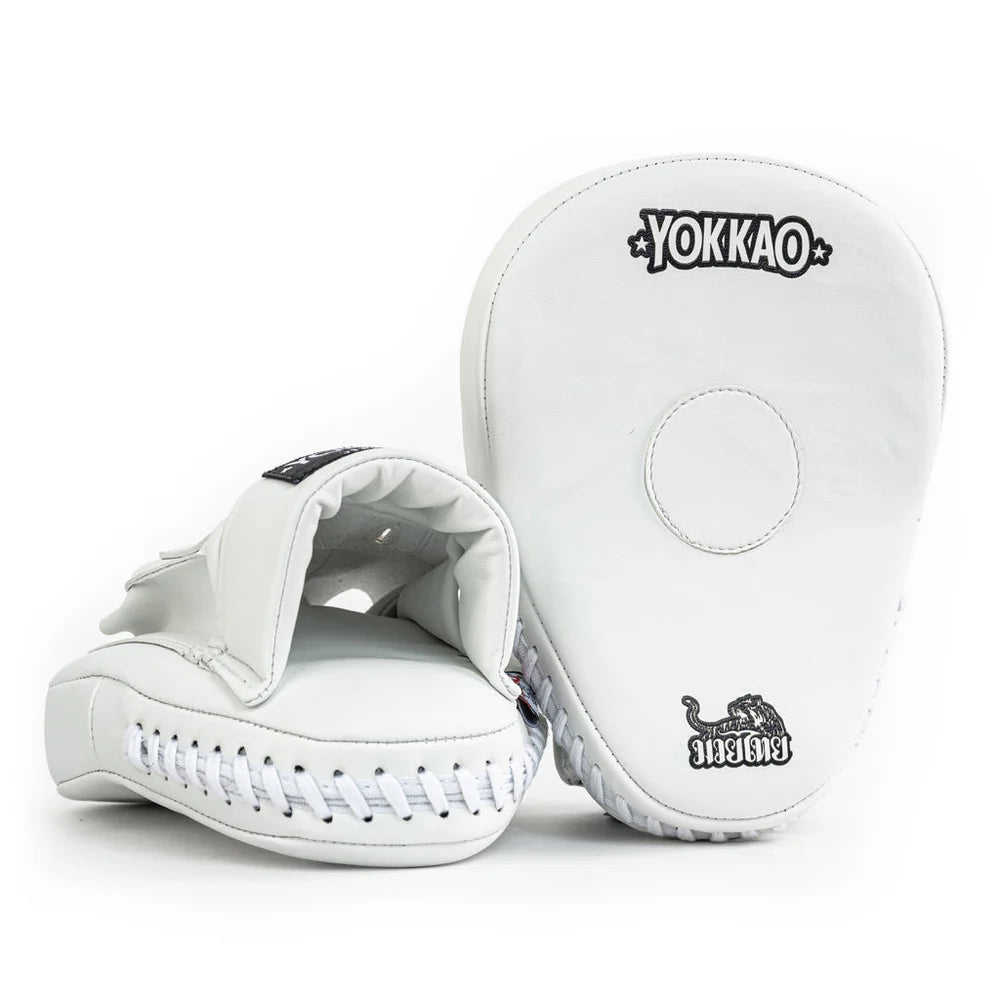 Yokkao focus mitts in wit met subtiele zwarte logo’s, gefotografeerd tegen een witte achtergrond. Rechts de voorzijde met rond doelvlak, links de open handinvoer met zachte padding en witte veters langs de onderzijde. Ontworpen voor nauwkeurige bokstraining en Muay Thai padsessies in de gym.
