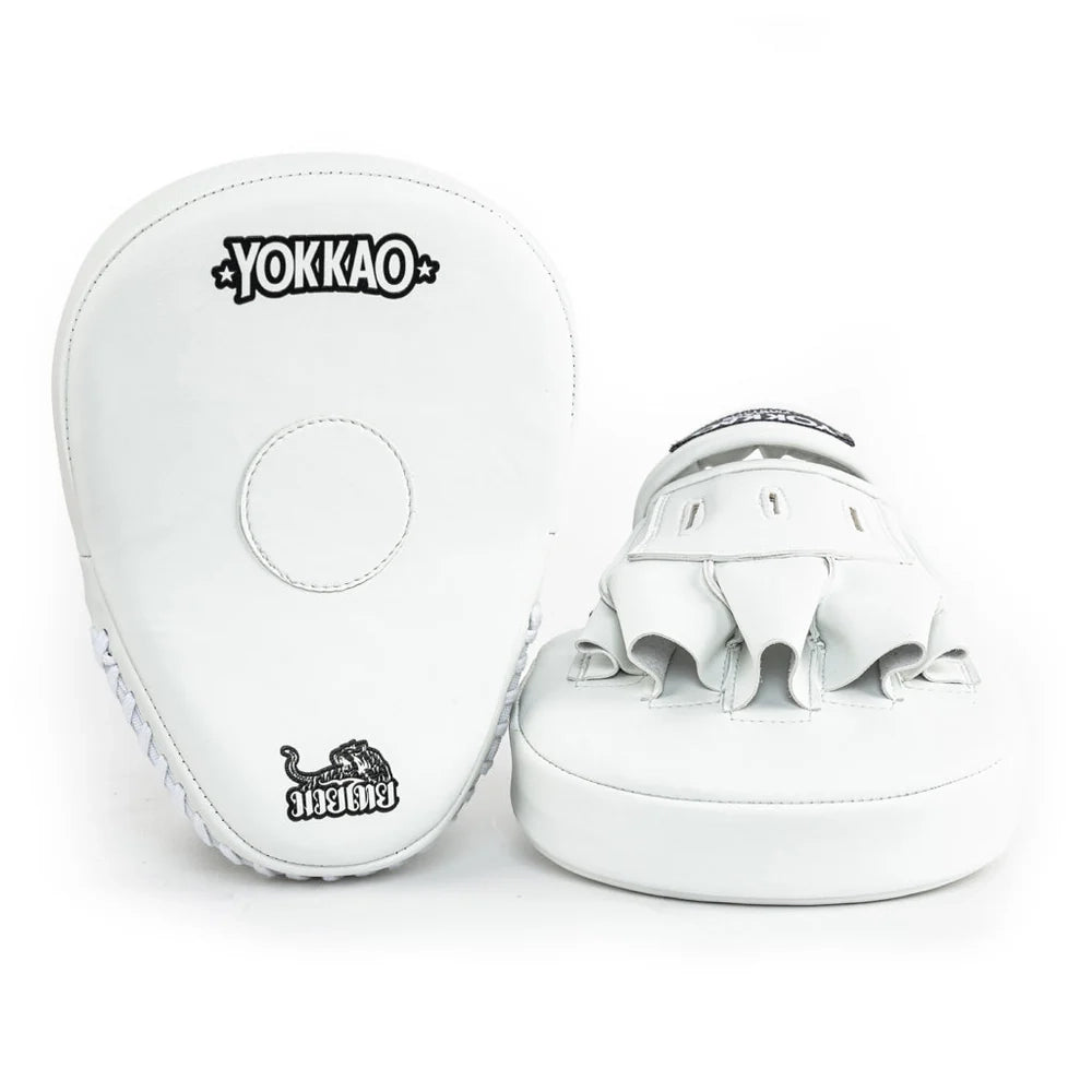 Yokkao focus mitts in wit, gefotografeerd tegen een witte achtergrond met zicht op voor- en achterzijde. Links de voorkant met rond doelvlak en Muay Thai-embleem, rechts de handinvoer met open vingers en dikke padding. Ideaal voor nauwkeurige padstraining tijdens boksen en Muay Thai in de gym.