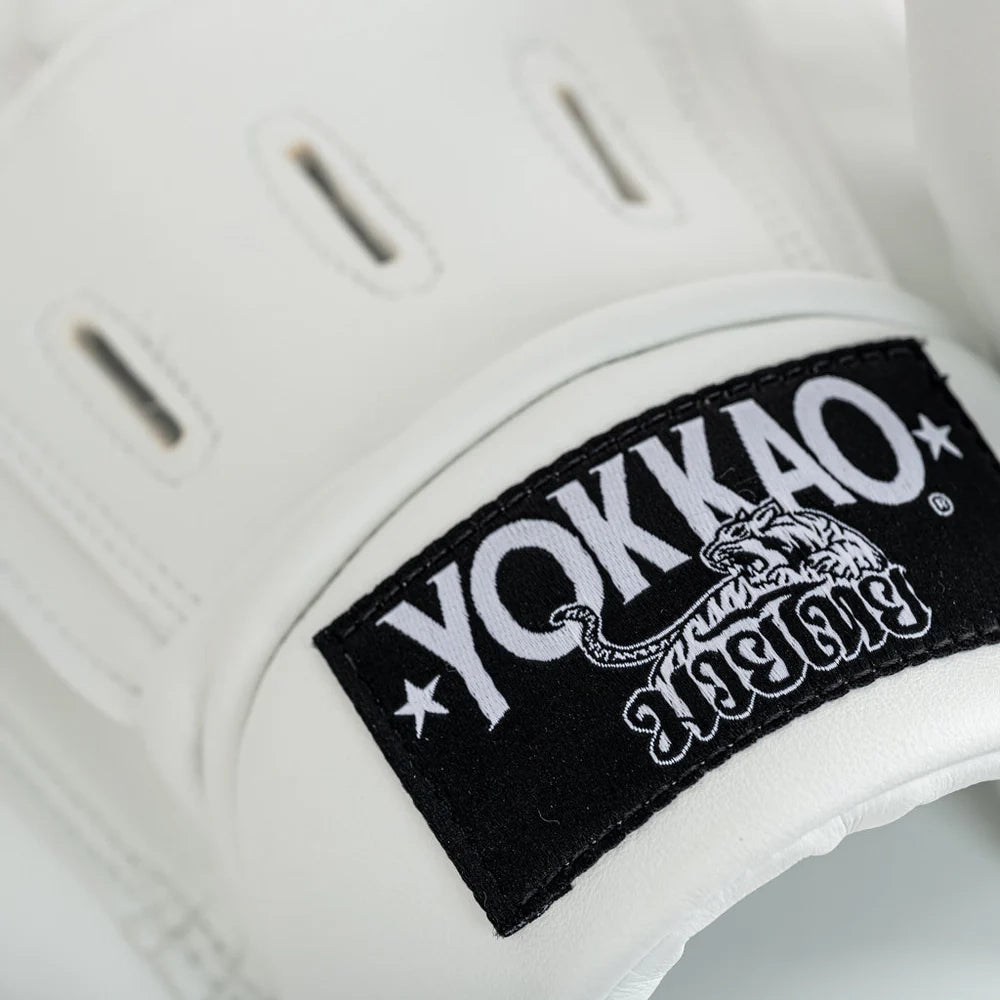 Close-up van Yokkao focus mitt in wit met zwart YOKKAO-logo op de polsband. De afbeelding toont de ventilatiesleuven bovenop en de stevige stiksels rondom de rand. Geschikt voor intensieve padstraining tijdens boksen en Muay Thai in de gym.