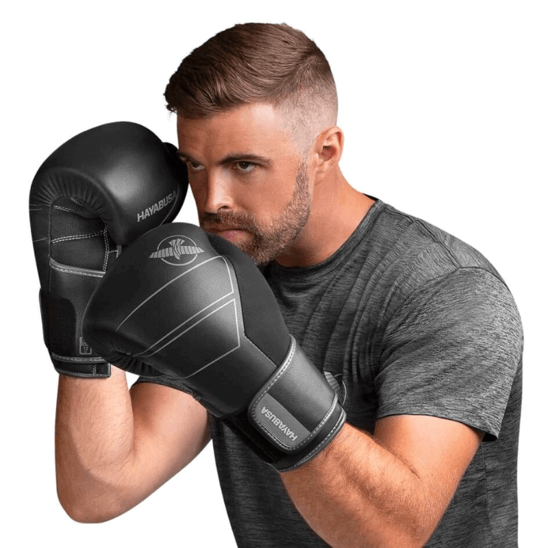 Een man met een donkergrijs shirt poseert met de Hayabusa Bokshandschoenen S4 Leather in zwart, klaar in een bokshouding met de handschoenen ter hoogte van zijn gezicht.