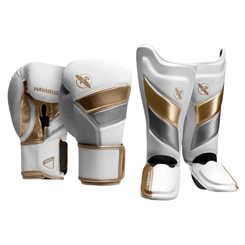 Een paar witte en gouden Hayabusa bokshandschoenen en scheenbeschermers, gericht op gevechtssport.