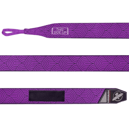 Een volledig uitgestrekte Hayabusa Perfect Stretch Bandage Purple Lotus met een herhalend lotuspatroon. Het bevat de tekst "THIS SIDE UP" aan het ene uiteinde en een zwart klittenbandstuk aan het andere uiteinde, naast het Hayabusa-logo.