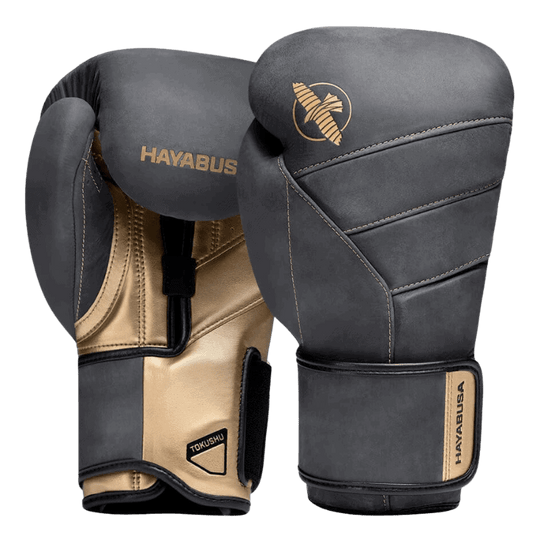 Een paar Hayabusa T3 LX Obsidian bokshandschoenen met gouden accenten op de bovenkant, waarbij één handschoen de klittenbandsluiting toont en de ander de gevoerde rug.