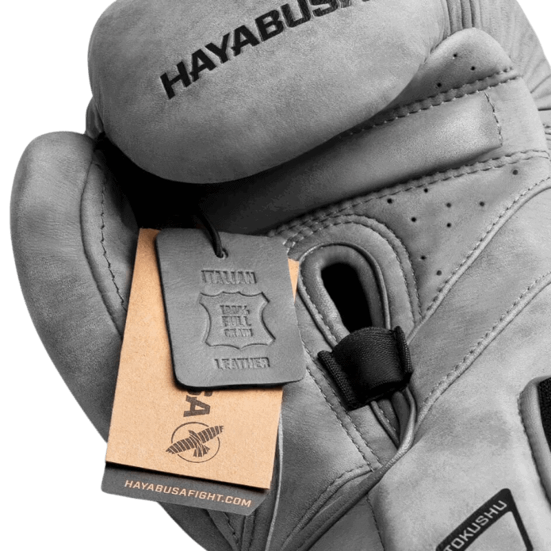 Detail van een Hayabusa T3 LX Slate bokshandschoen waarbij het kwaliteitslabel toont "PREMIUM FULL GRAIN LEATHER", met de handschoen licht gebogen om de vorm te tonen.