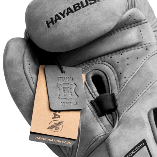Detail van een Hayabusa T3 LX Slate bokshandschoen waarbij het kwaliteitslabel toont "PREMIUM FULL GRAIN LEATHER", met de handschoen licht gebogen om de vorm te tonen.