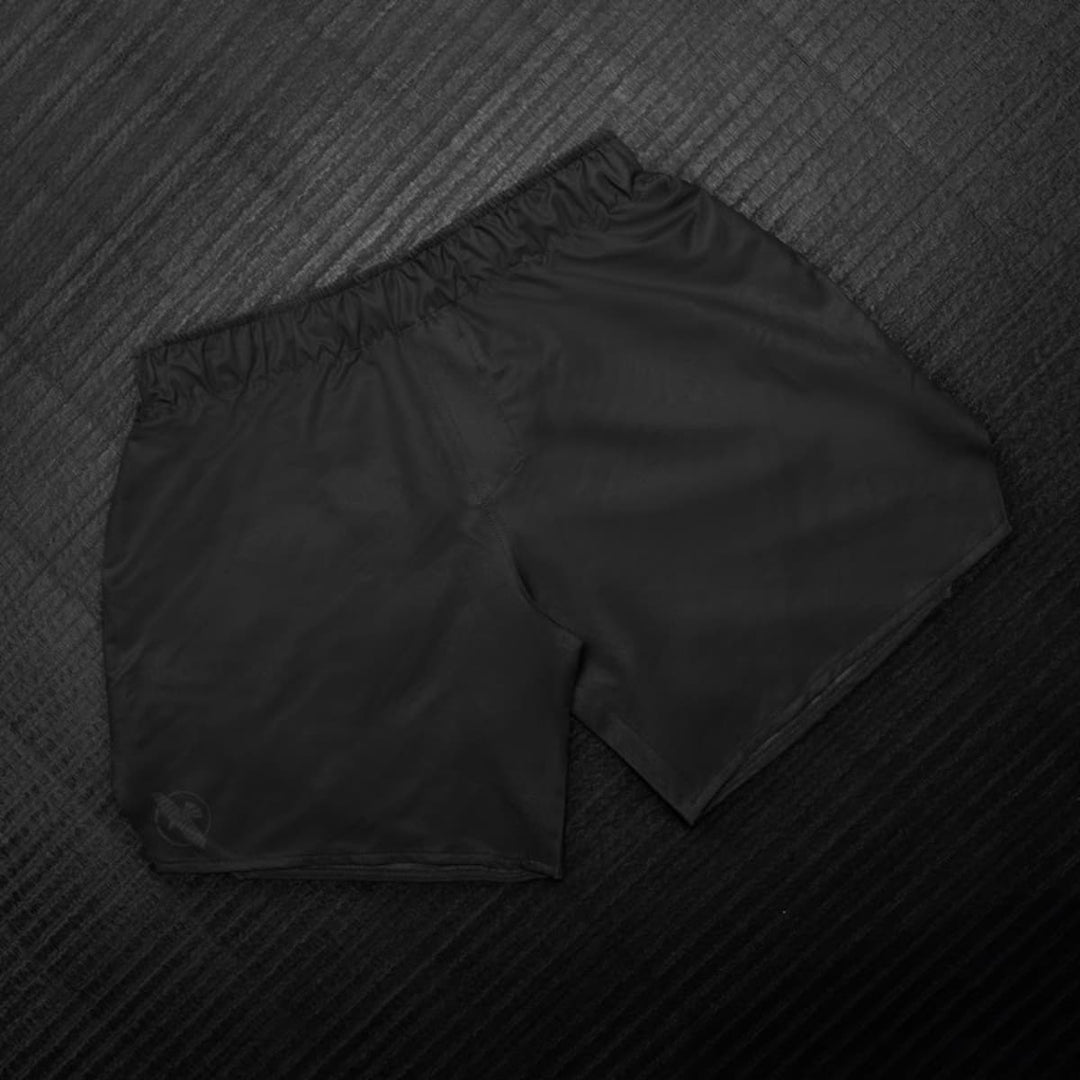 Hayabusa MMA Shorts Heren Core Zwart liggend gefotografeerd met volledig overzicht van het minimalistische ontwerp.