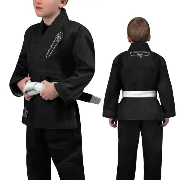 Jonge vechter in zwarte Hayabusa Essential Youth BJJ Gi met witte band, voor- en achteraanzicht van het duurzame jiu-jitsu pak voor kinderen met wit logo.