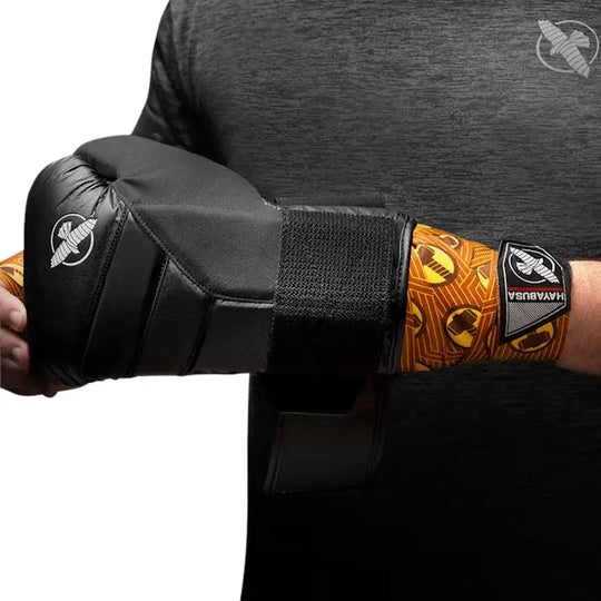 Hayabusa Thor bandage in oranje-geel design zichtbaar onder zwarte bokshandschoen, man in grijs sportshirt houdt handschoen vast.