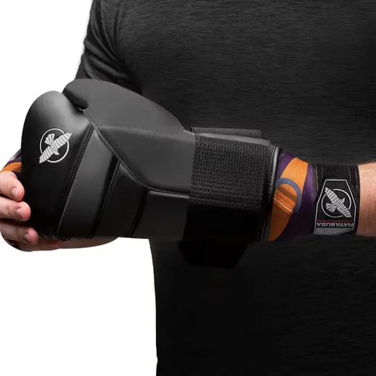 Man die bokshandschoenen aantrekt over paarse en oranje Hayabusa Batroc-bandages om de pols.