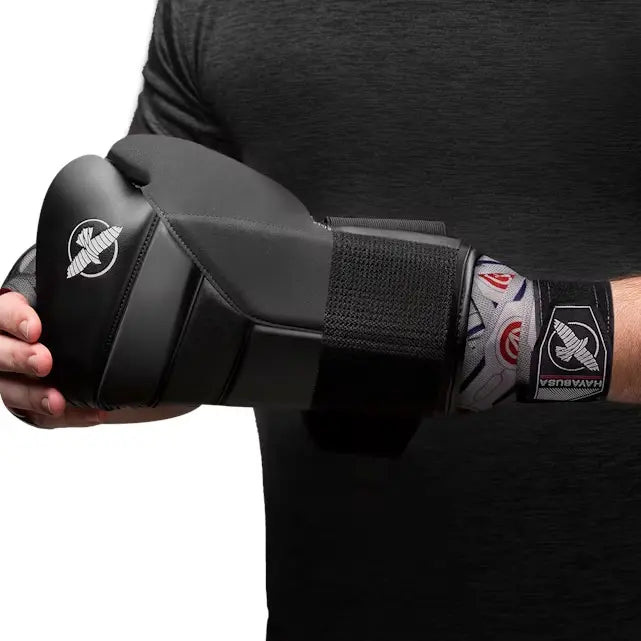 Grijze Hayabusa handwraps met Falcon- en Avengers-logo’s zichtbaar onder zwarte bokshandschoen, gedragen door sporter in zwart shirt tijdens het vastmaken van de handschoen.