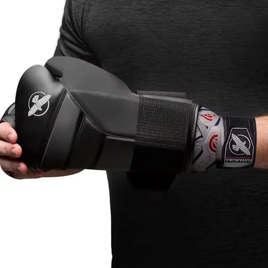 Grijze Hayabusa handwraps met Falcon- en Avengers-logo’s zichtbaar onder zwarte bokshandschoen, gedragen door sporter in zwart shirt tijdens het vastmaken van de handschoen.