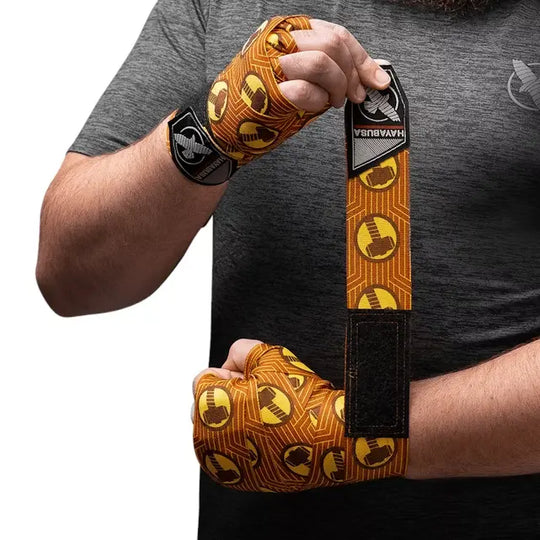 Hayabusa Thor bandages om beide handen gewikkeld, oranje-geel design met hamerprint, man rolt bandage af in grijs sportshirt.