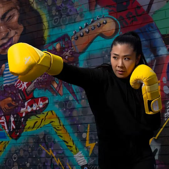 Vrouw traint met gele Hayabusa T3 bokshandschoenen en stoot naar voren voor een kleurrijke graffitiwand.