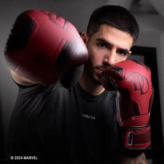 Een man dat een stoot uitvoert met de rode Hayabusa Bokshandschoenen uit de Marvel Daredevil-collectie, duidelijk zichtbaar is het Daredevil 'DD' logo op de knokkel.