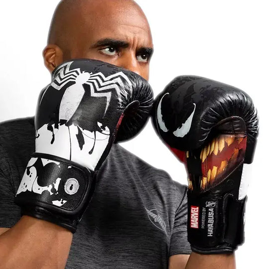 Een man met kaalgeschoren hoofd toont twee zwarte bokshandschoenen met een Marvel Venom-thema, één met het spinnenlogo en de ander met de tanden van Venom.