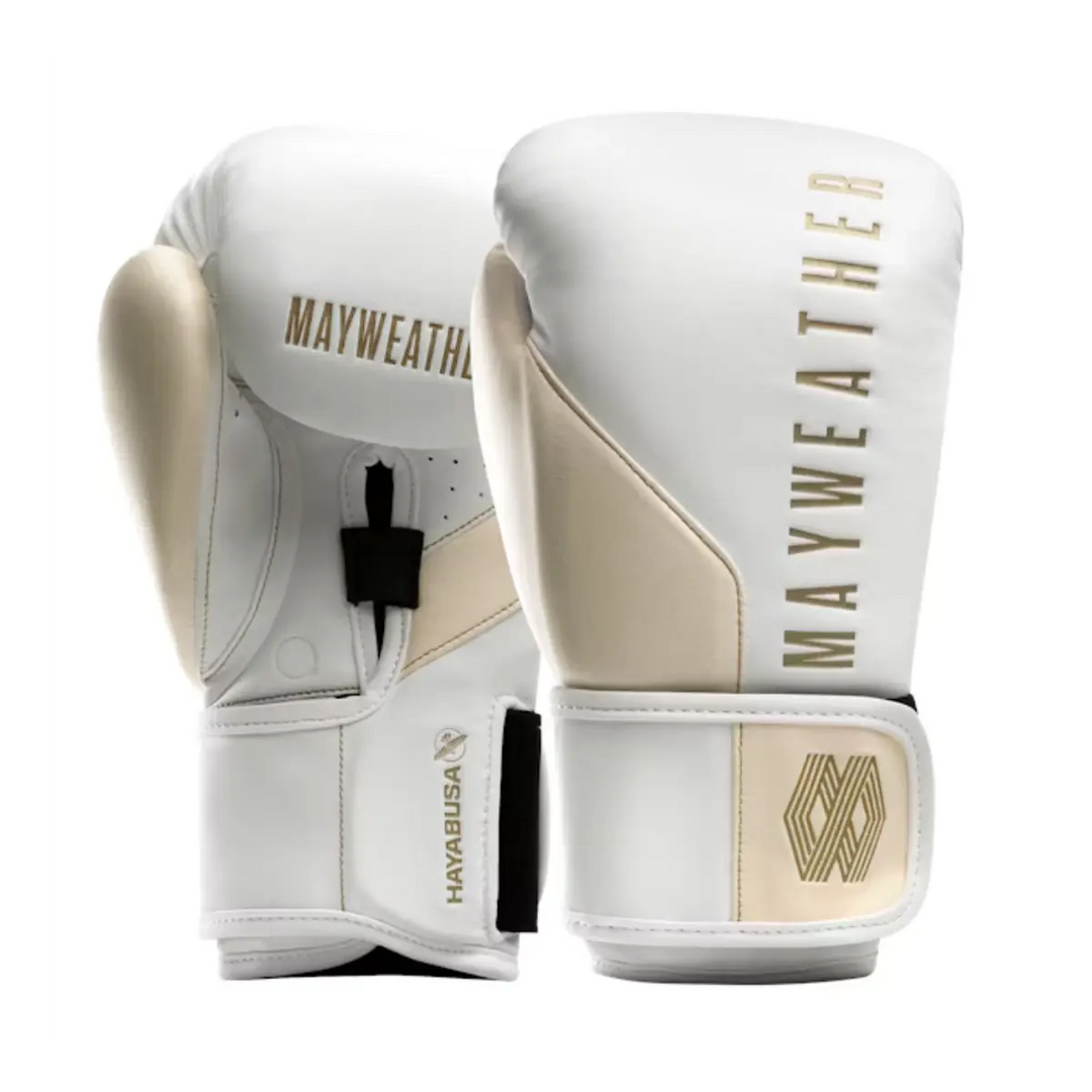 Een paar witte boks- of MMA-handschoenen met goudkleurige accenten en het Mayweather-logo in goud staat rechtop. De handschoenen, een samenwerking met Hayabusa, hebben een goudkleurige duim en een bijpassend geometrisch logo op de polsband.