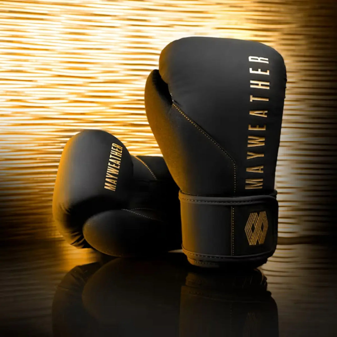 Zwarte Mayweather bokshandschoenen met gouden accenten en glanzende achtergrond, symbool voor luxe, kracht en precisie in professioneel boksen.