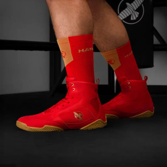 Achteraanzicht van rode Hayabusa boksschoenen met bruine zolen gedragen met rode sokken in gym met Hayabusa branding.