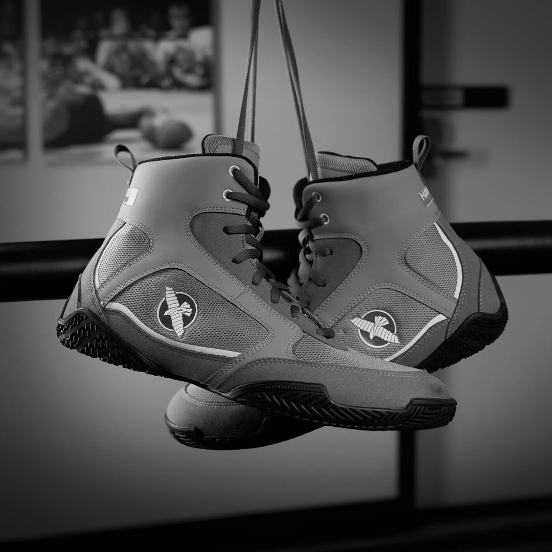 Grijze Hayabusa Pro boksschoenen hangend aan de veters in een trainingsruimte. De hoge enkelsteun, meshpanelen en zwarte gripzool maken de schoenen geschikt voor boksers die stabiliteit, ventilatie en controle zoeken tijdens hun training.