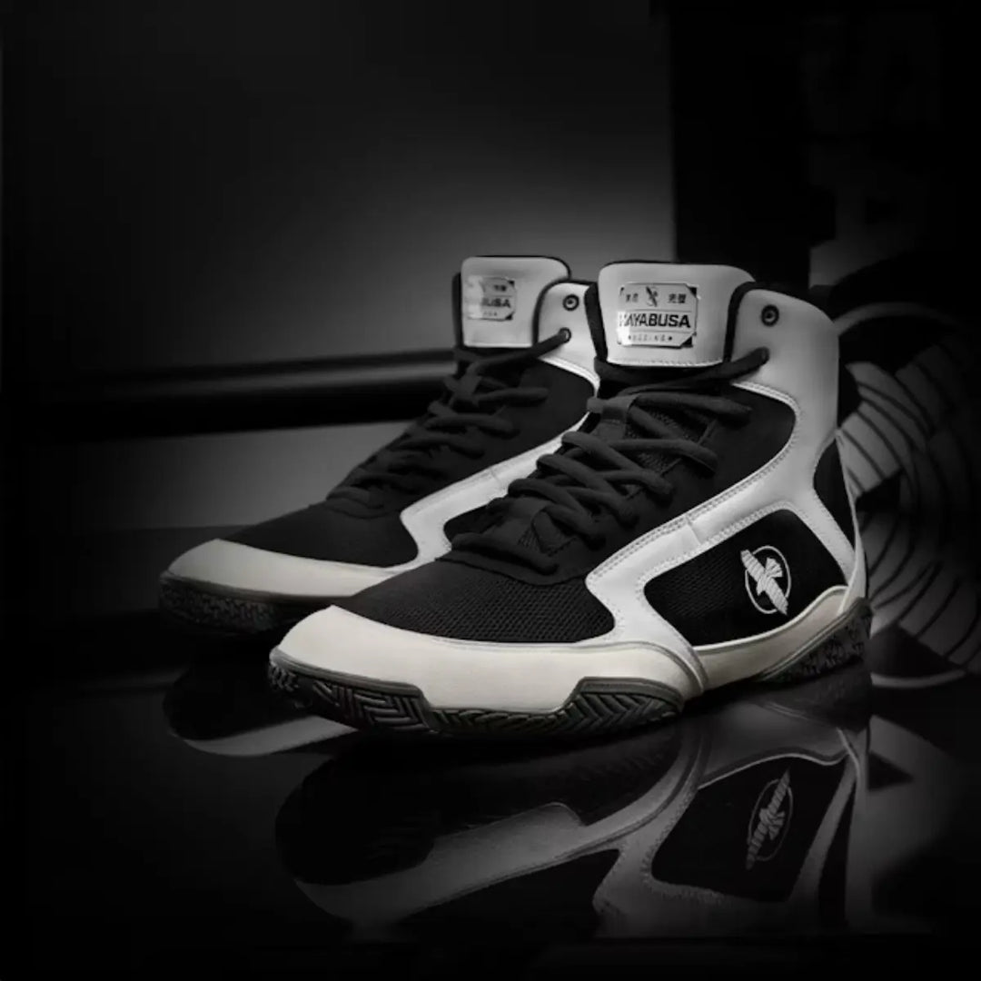 Zwarte en witte Hayabusa boksschoenen gepresenteerd op glanzende zwarte ondergrond met studioverlichting.