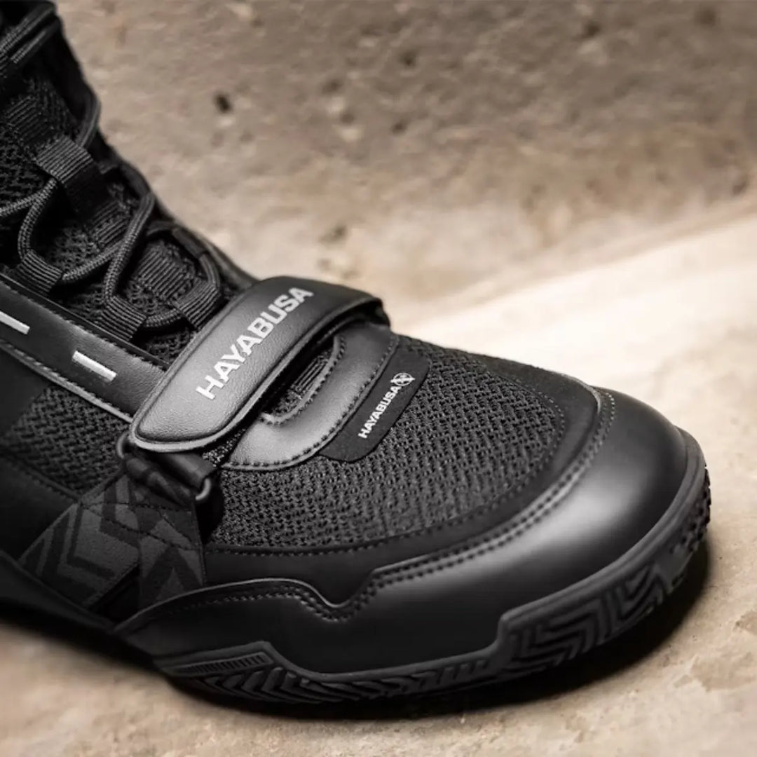Close-up van de zwarte Hayabusa boksschoen met ademend mesh, stevige neusbescherming en verstelbare strap voor optimale pasvorm en stabiliteit tijdens intensieve bokstraining.