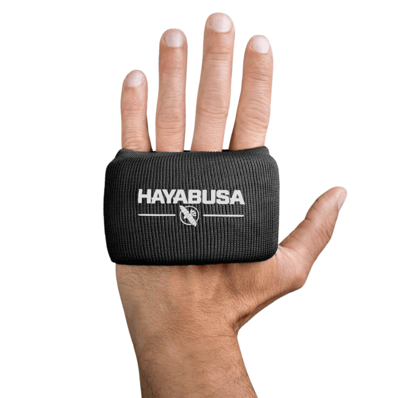Een hand met de palm naar de camera gericht waarbij een zwarte Hayabusa Boxing Knuckle Guard wordt gedragen, met het witte Hayabusa-logo en adelaarsembleem bovenop de hand.
