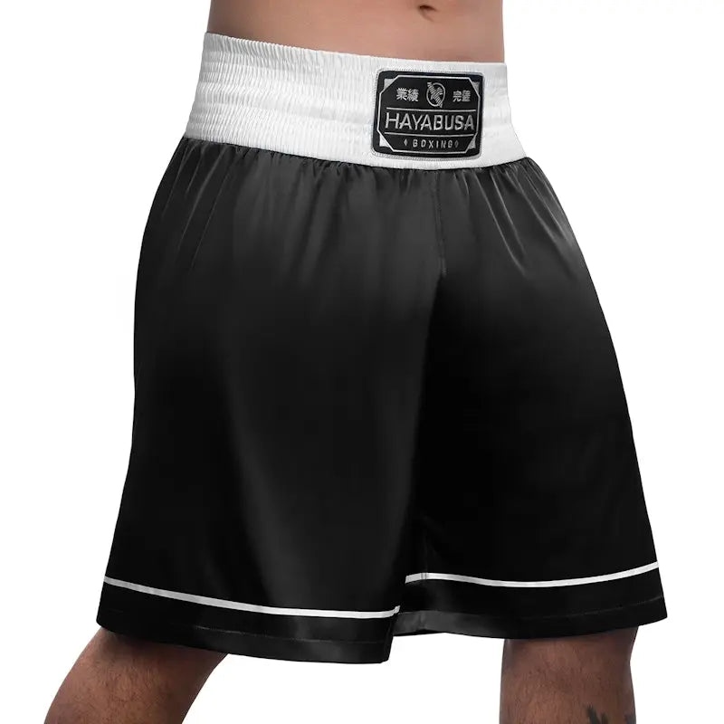Front right view of black Hayabusa boxing shorts with a wide white elastic waistband and stitched Hayabusa Boxing patch. The lightweight, smooth fabric and white trim along the hem emphasize mobility, comfort, and a clean, professional boxing style.