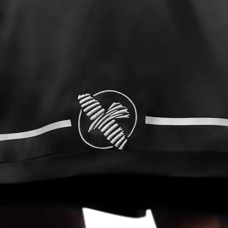 Detail shot of the embroidered Hayabusa falcon logo on black boxing shorts, positioned above the hem with subtle white accent lines. The contrast stitching and smooth fabric texture emphasize the clean design, durability, and professional boxing style.