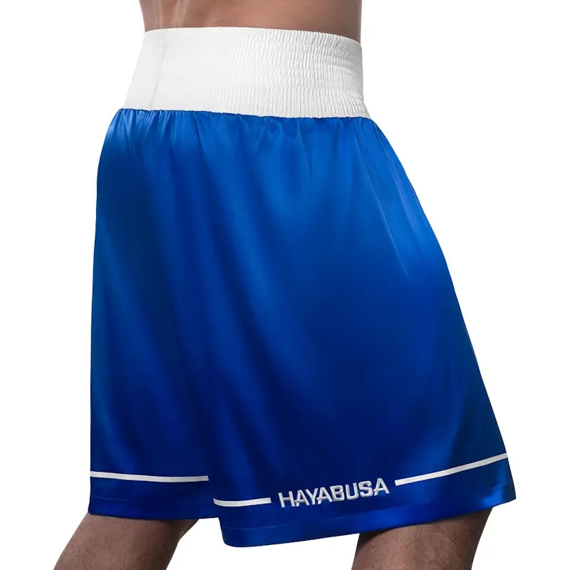 Rear view of blue Hayabusa boxing shorts with a wide white elastic waistband and subtle white trim near the hem. The smooth, lightweight fabric drapes comfortably for unrestricted movement, while the Hayabusa logo at the back adds a clean, professional finish ideal for boxing training and competition.