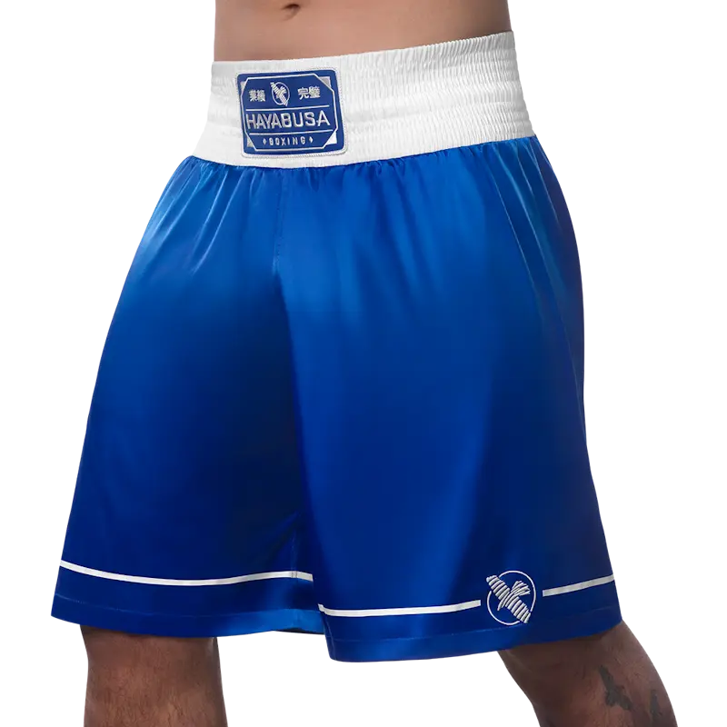 Front left view of blue Hayabusa boxing shorts with a wide white elastic waistband and Hayabusa Boxing patch. The smooth satin-style fabric, white piping along the hem, and embroidered Hayabusa logo highlight a classic boxing design with excellent comfort and freedom of movement.