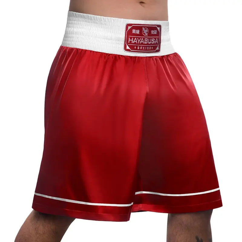 Front view of red Hayabusa boxing shorts featuring a wide white elastic waistband with a stitched Hayabusa Boxing patch. The satin fabric has a smooth finish with subtle white trim along the hem. The relaxed cut highlights freedom of movement and a classic boxing style suitable for training and gym sessions.