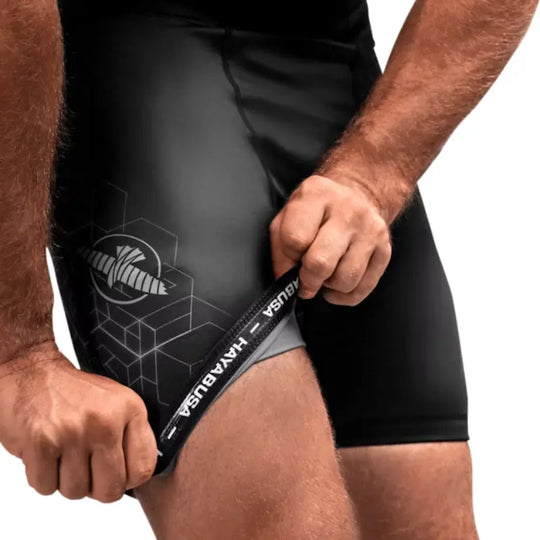 Close-up van zwarte Hayabusa compressieshort met grijs logo en grafische print, sporter trekt de pijp iets omhoog om de pasvorm te tonen.