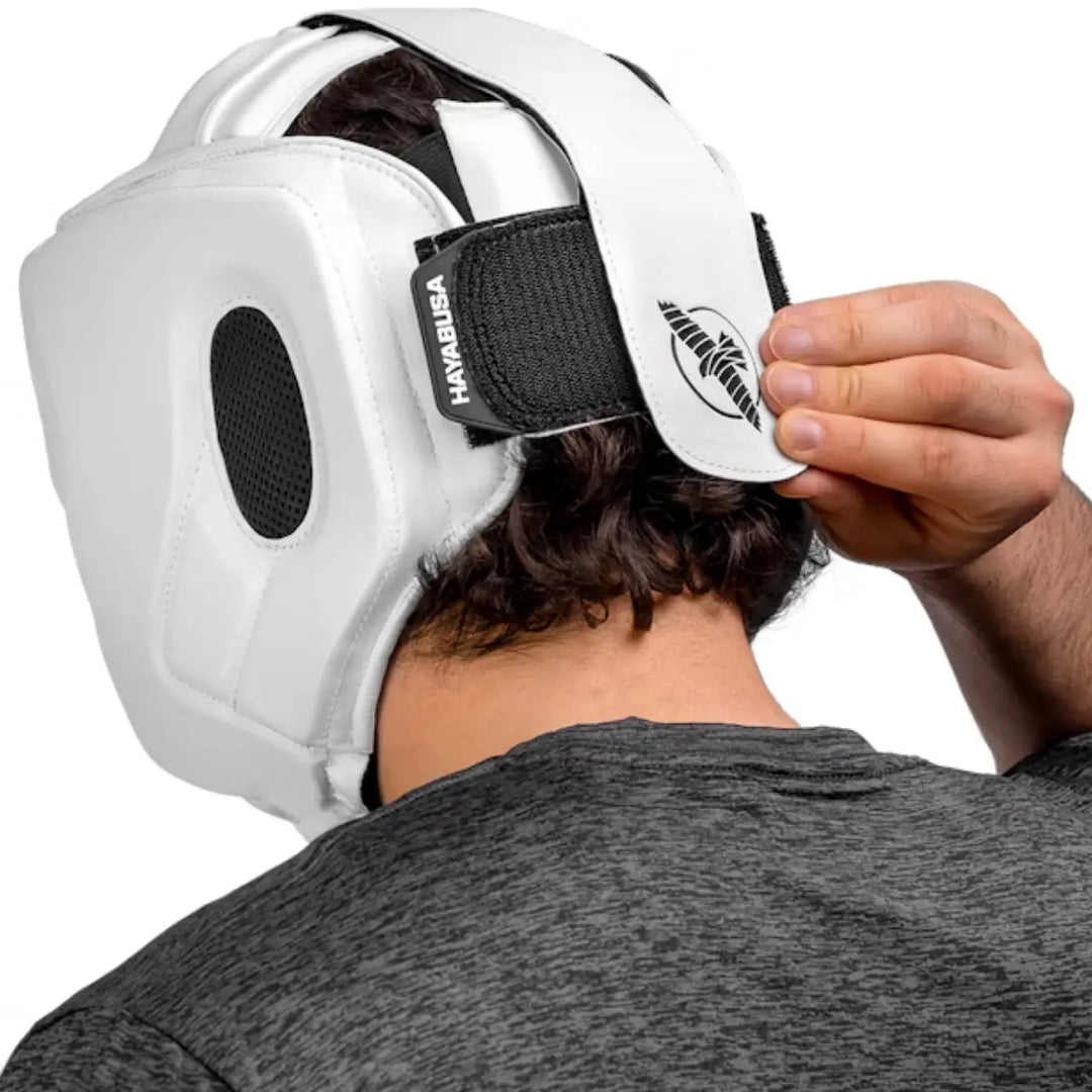 Man stelt de verstelbare sluiting af van een witte Hayabusa hoofdbeschermer met zwart logo.