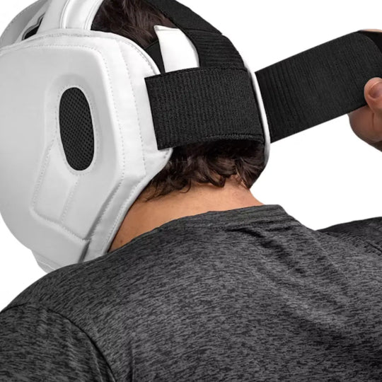 Man bevestigt een witte Hayabusa hoofdbeschermer met brede zwarte klittenbandsluiting aan de achterkant voor een stevige pasvorm.