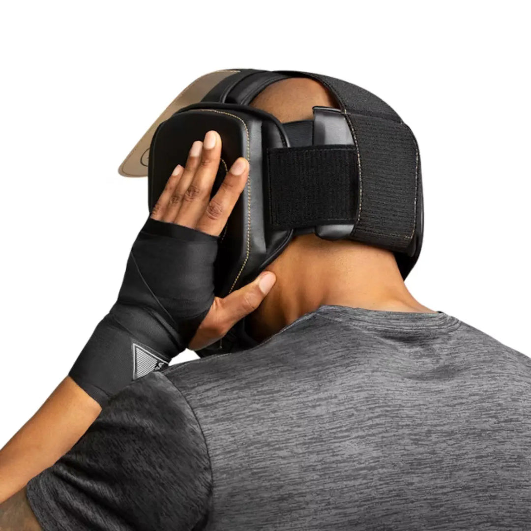 Vechter past zwarte Hayabusa hoofdbeschermer met gouden details en klittenbandsluiting aan tijdens training.