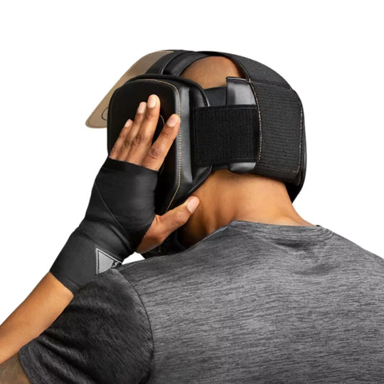 Vechter past zwarte Hayabusa hoofdbeschermer met gouden details en klittenbandsluiting aan tijdens training.