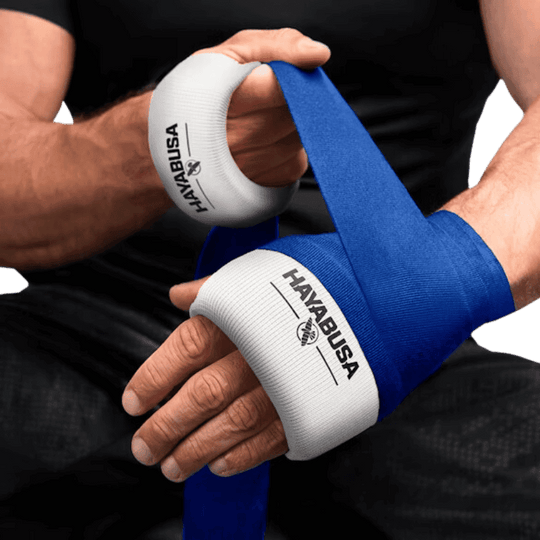 Een persoon wikkelt een blauwe bandage over een witte Hayabusa handwrap om de pols.