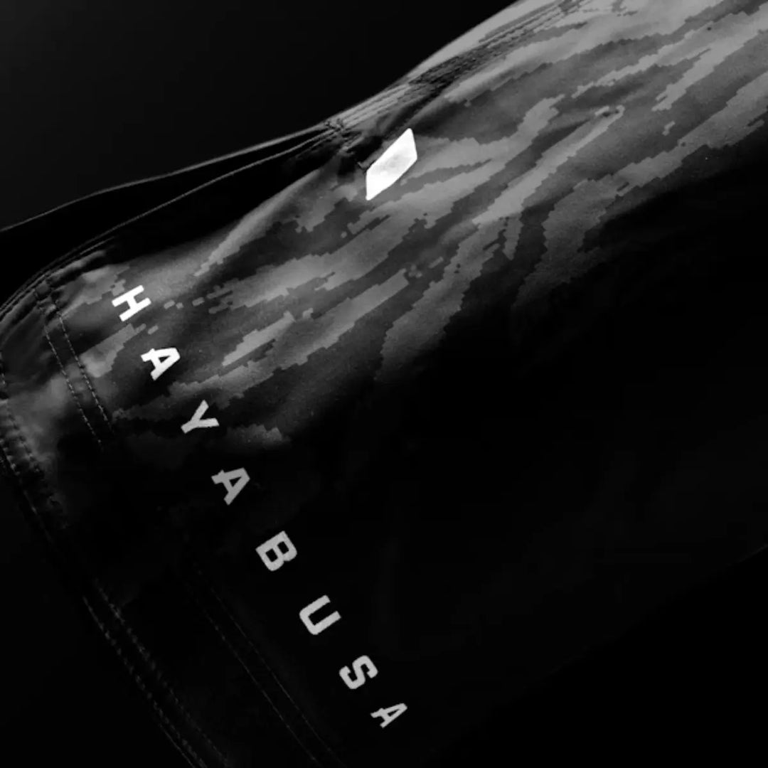Close-up van zwarte Hayabusa fightshorts met subtiel camo-patroon en wit logo op de pijp.