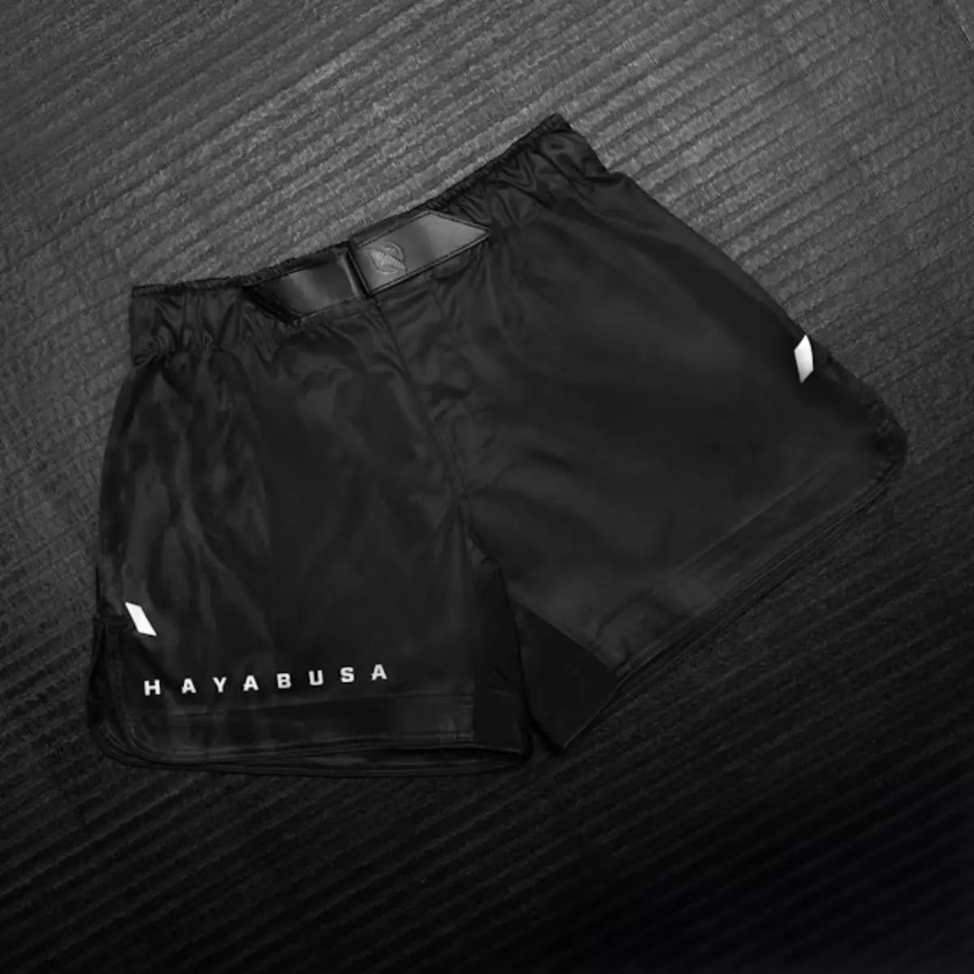 Zwarte Hayabusa fightshorts met subtiel logo op de pijp, liggend op een mat met textuur.