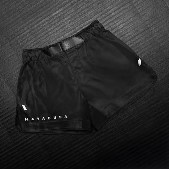 Zwarte Hayabusa fightshorts met subtiel logo op de pijp, liggend op een mat met textuur.