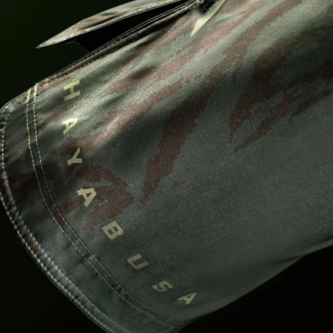 Close-up van groene Hayabusa MMA fightshorts met subtiel camouflagedesign en opdruk van de merknaam langs de zoom.