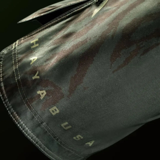 Close-up van groene Hayabusa MMA fightshorts met subtiel camouflagedesign en opdruk van de merknaam langs de zoom.