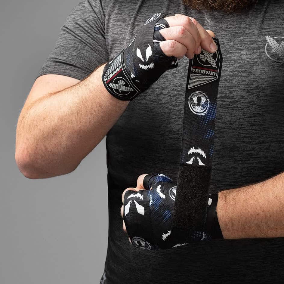 Een persoon wikkelt een zwarte en blauwe Hayabusa handbandage, met een Marvel Symbiote patroon, om zijn hand.