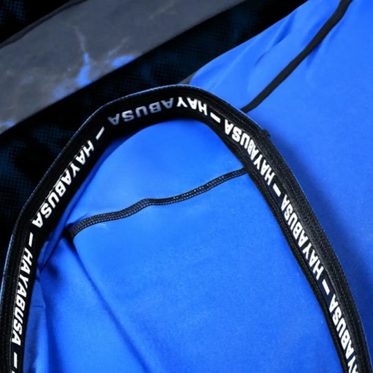 Detailfoto van de binnenkant van de rashguard, waar de zwarte antislip-gripband met het witte HAYABUSA-logo zichtbaar is. De felblauwe stof toont de gladde, hoogwaardige afwerking. De afbeelding benadrukt de stevige pasvorm en functionaliteit van de gripband tijdens training.